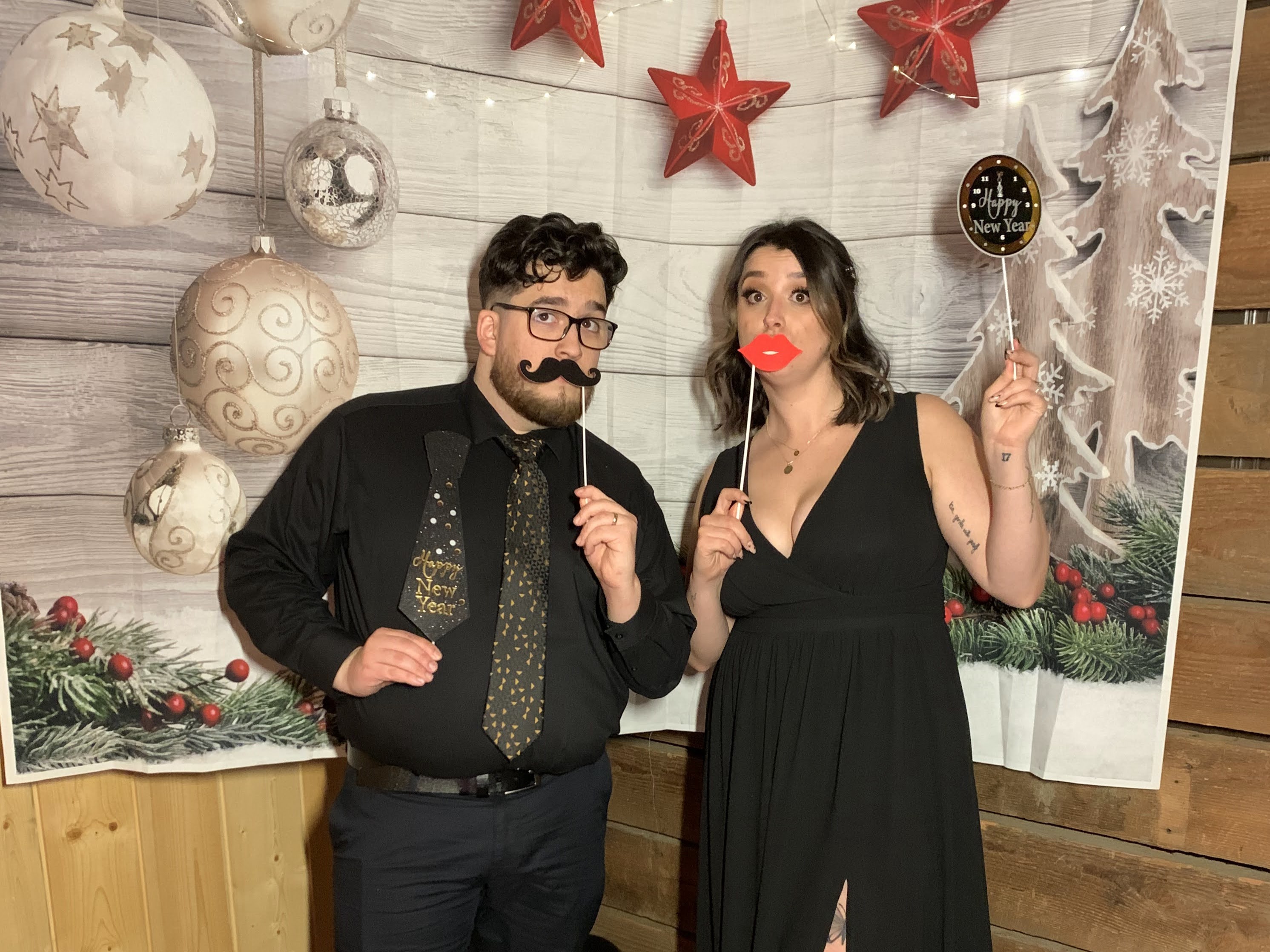 My wife and I posing with some goofy happy new years props. I'm wearing a black dress shirt, tie, and pants. My wife is wearing a black dress.